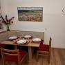 Dining area with corner bench, table and chairs, set with crockery. On the wall, a picture of poppies and a quote with butterflies.