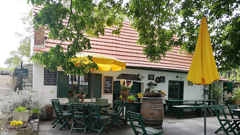 Cozy guest garden with yellow parasol and wooden tables in front of a building with a red tiled roof.