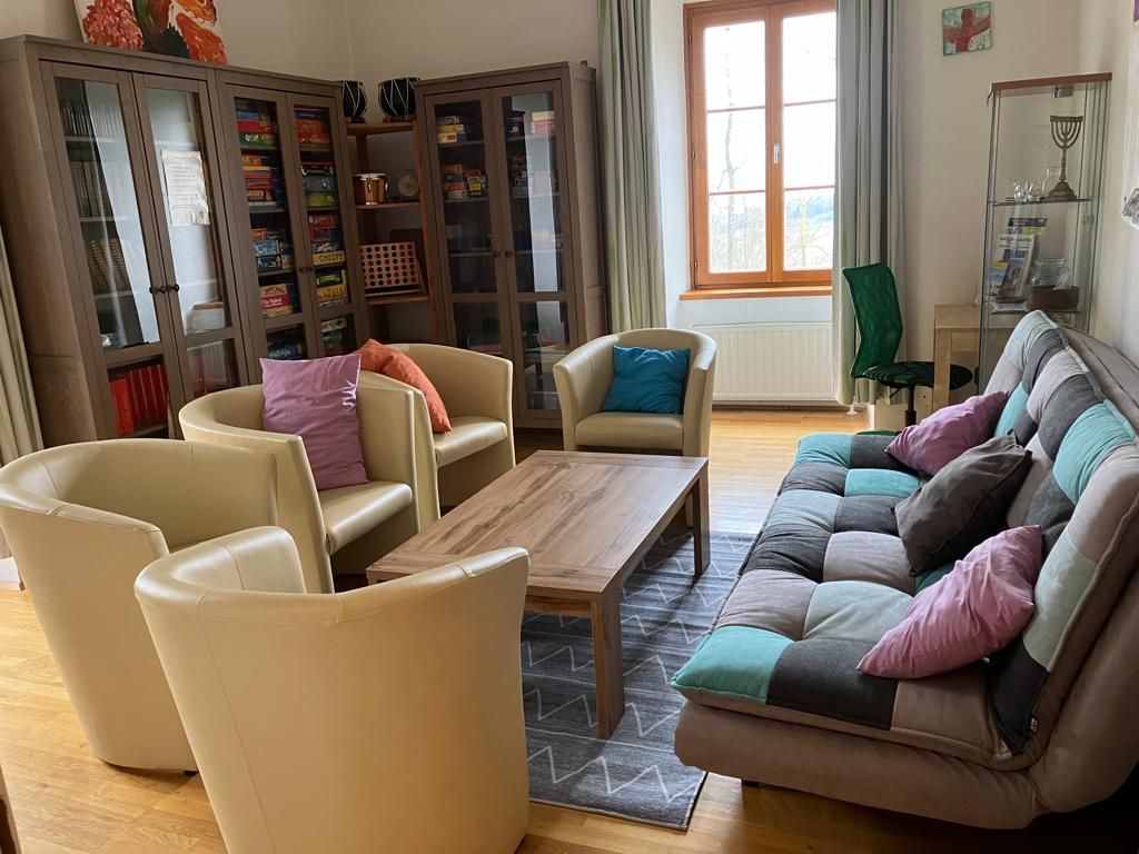 A cozy common room with armchairs, a sofa, a table and bookshelves.