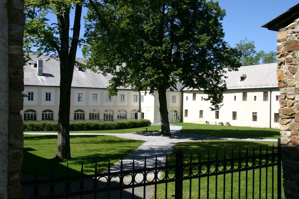 A well-kept castle courtyard with a large tree in the middle, surrounded by a historic building with white walls and many windows.