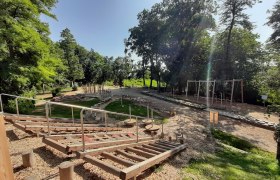 A motor skills park with various wooden elements and climbing equipment, surrounded by trees and green spaces.