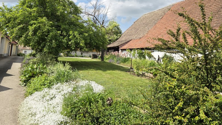 Rural scene with a cloudy sky, green meadow and a building with a red tiled roof.