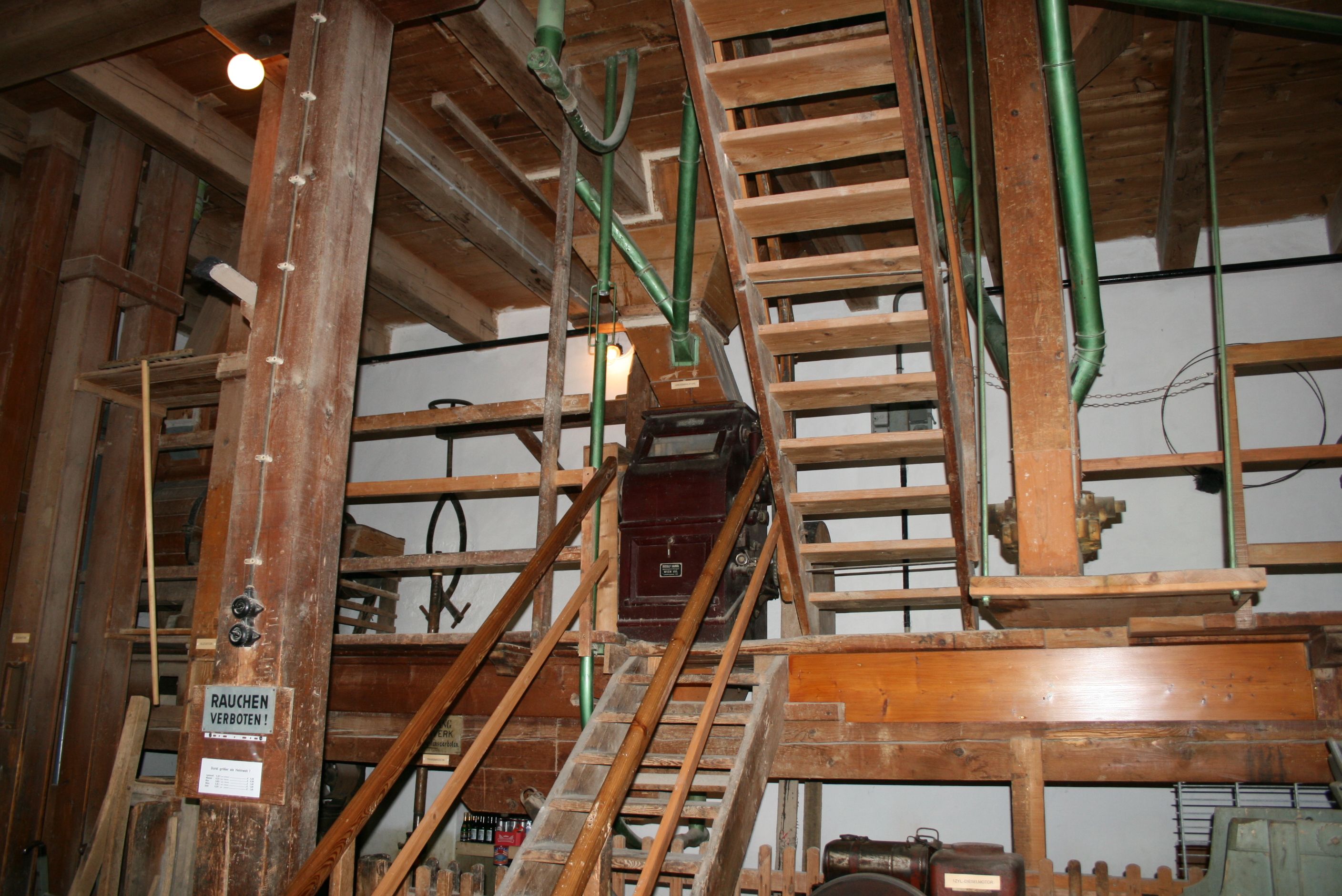 Interior view of an old mill with wooden stairs and machinery.