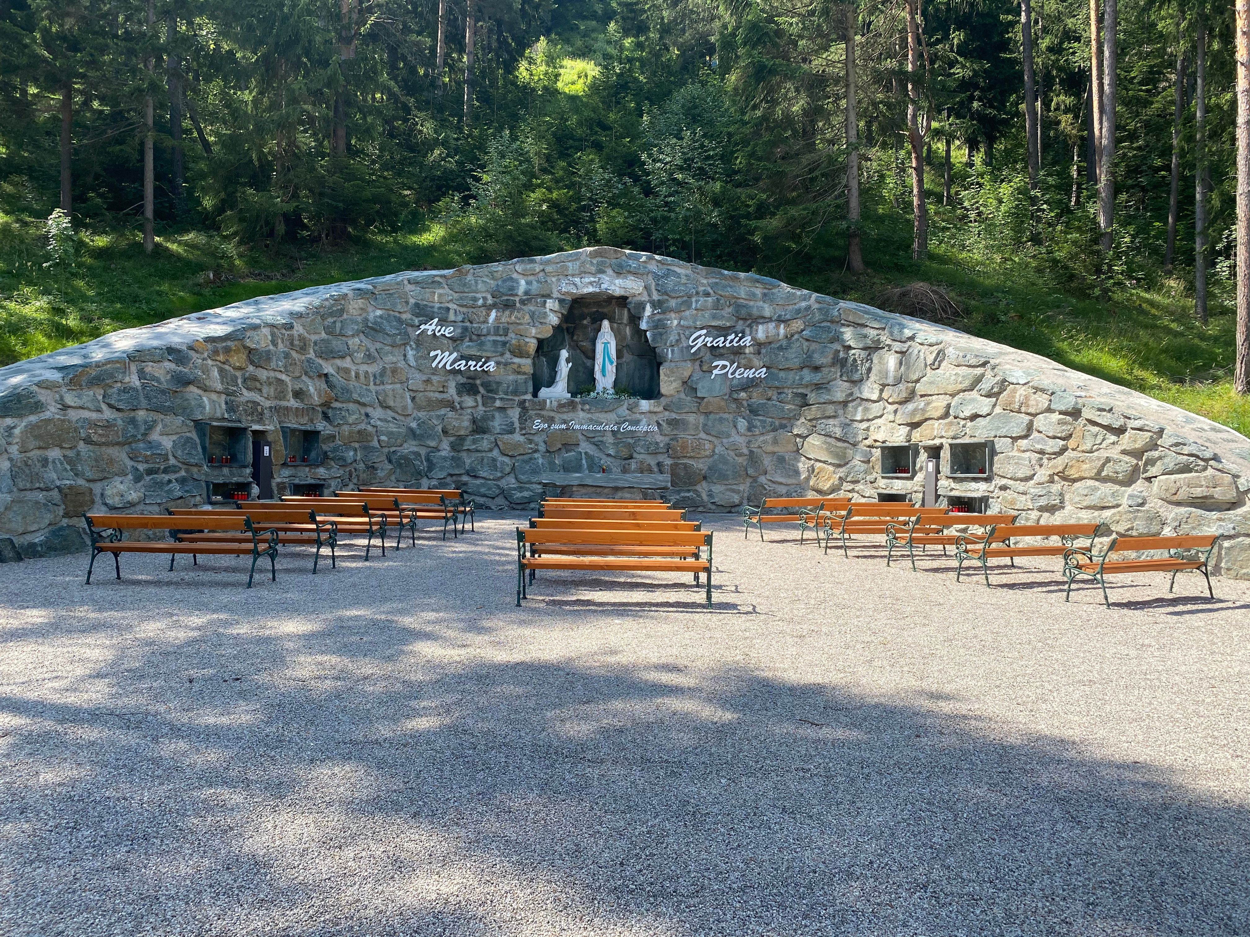 Stone grotto with a statue of the Virgin Mary and benches outside.
