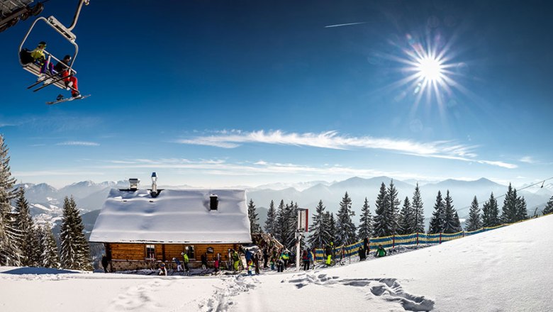 Winter landscape with ski hut, chair lift and mountains in the background.