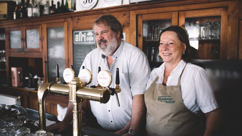 A man and a woman stand smiling behind a bar in a pub.