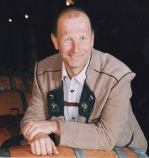 A man in traditional dress leans against a wine barrel.