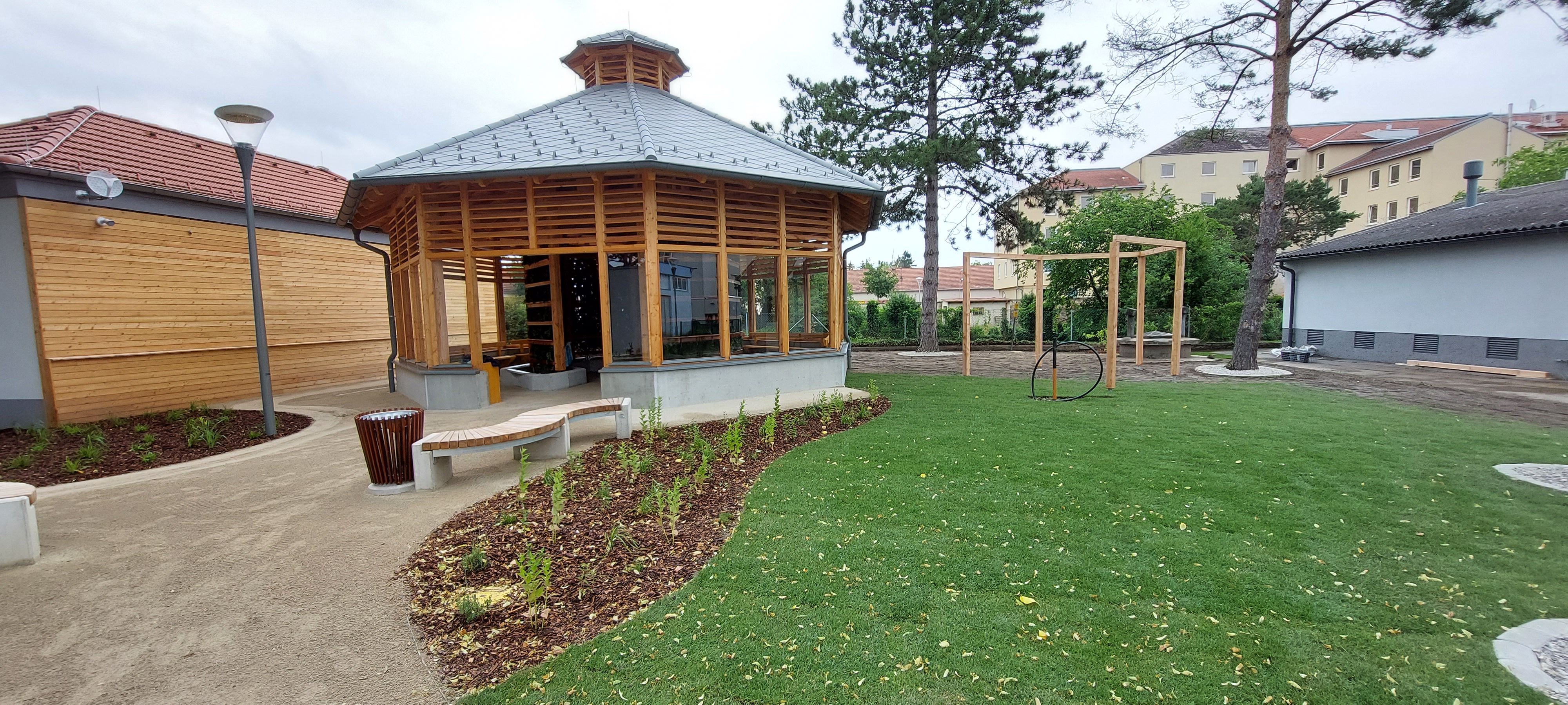A modern inhalatorium with wooden construction and glass windows in a well-tended garden with lawn and trees.