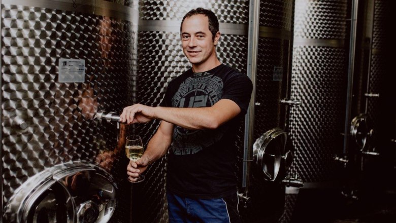 Man draws wine from a stainless steel tank in a wine cellar.
