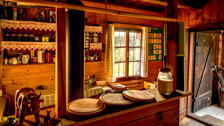 Cozy wooden hut with rustic furnishings, a window with curtains and an open door area.