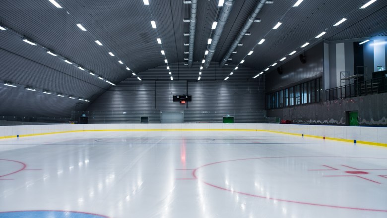 Empty ice rink with illuminated pitch and scoreboard.