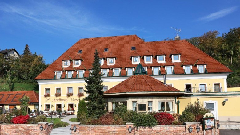 Exterior view of a yellow country hotel with a red roof and garden.