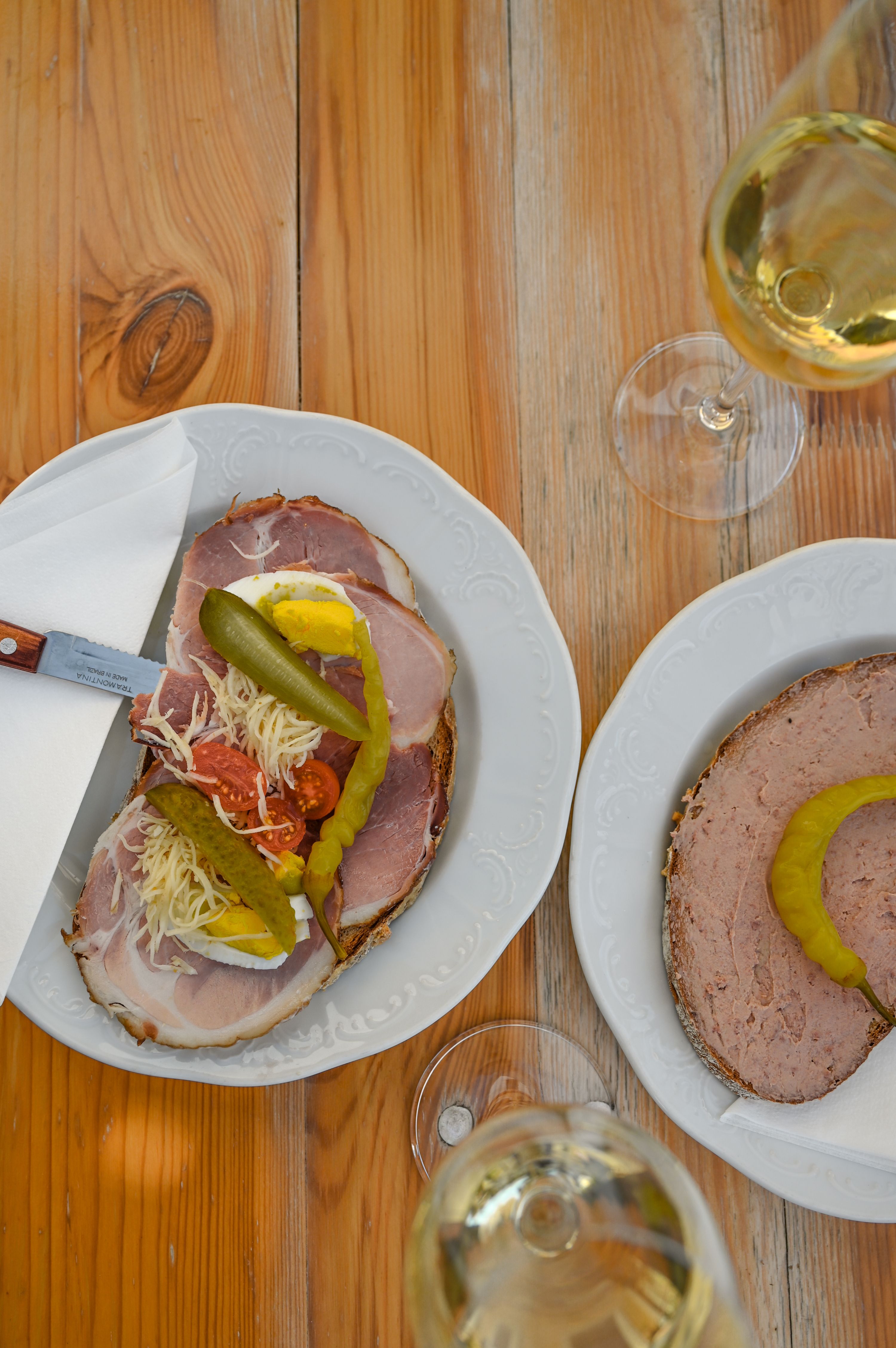 Two plates with sandwiches and two glasses of white wine on a wooden table.