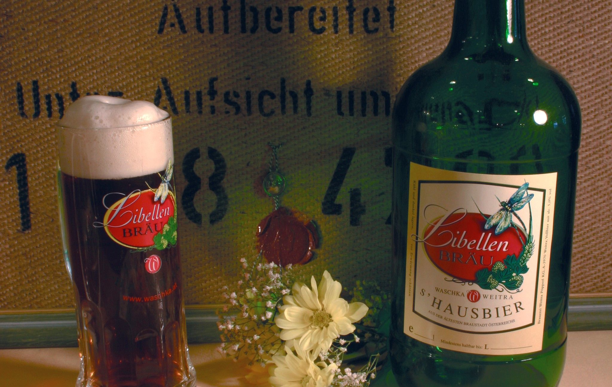 A glass and a bottle of Libellen Bräu beer with flowers in the foreground.