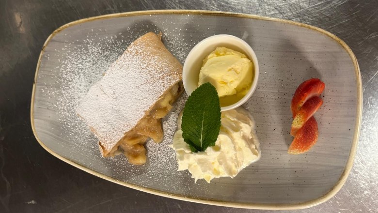 A dessert plate with apple strudel, vanilla ice cream, whipped cream and strawberry slices.