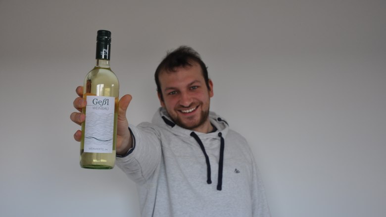 Man holding a bottle of Ge&szlig;l Weinbau white wine to the camera.