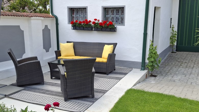 Terrace with rattan furniture and yellow cushions, surrounded by white walls and red flowers.