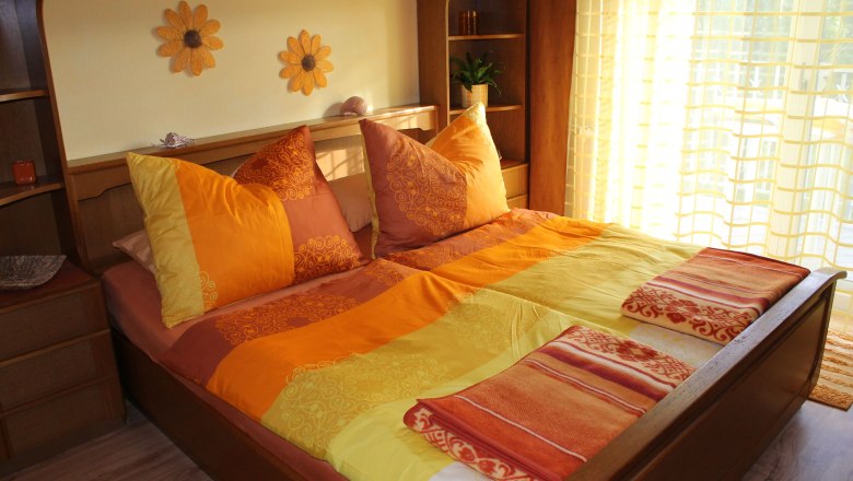 Cozy bedroom with sunflower decor and orange-yellow bed linen.
