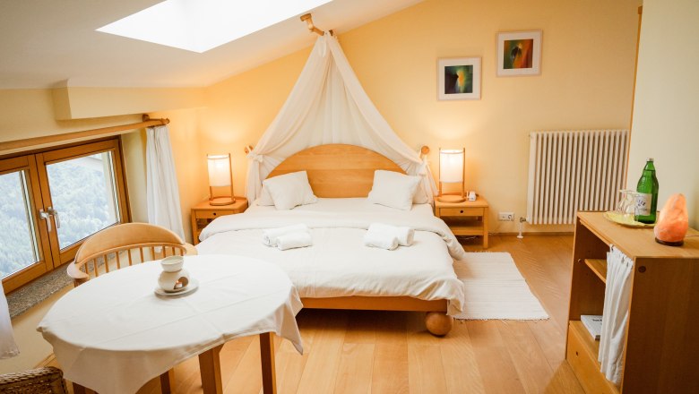 Cozy double room with wooden furniture, large bed, table and chairs, window with a view and soft lighting.