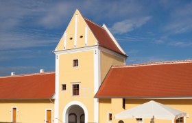 Yellow building with red roof and archway, blue sky in the background.