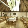 Interior view of a rustic room with wooden tables and chairs, a large skylight and decorative plants.
