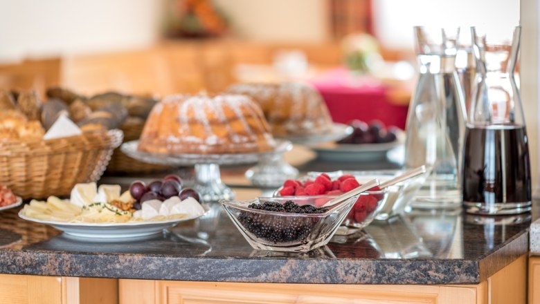 Breakfast buffet with cake, berries, cheese platter and drinks on a table.