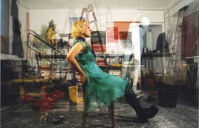 A woman in a green dress sits on a chair in a crowded room.