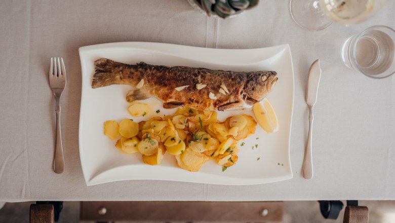 Trout with potatoes and lemon served on a white plate.