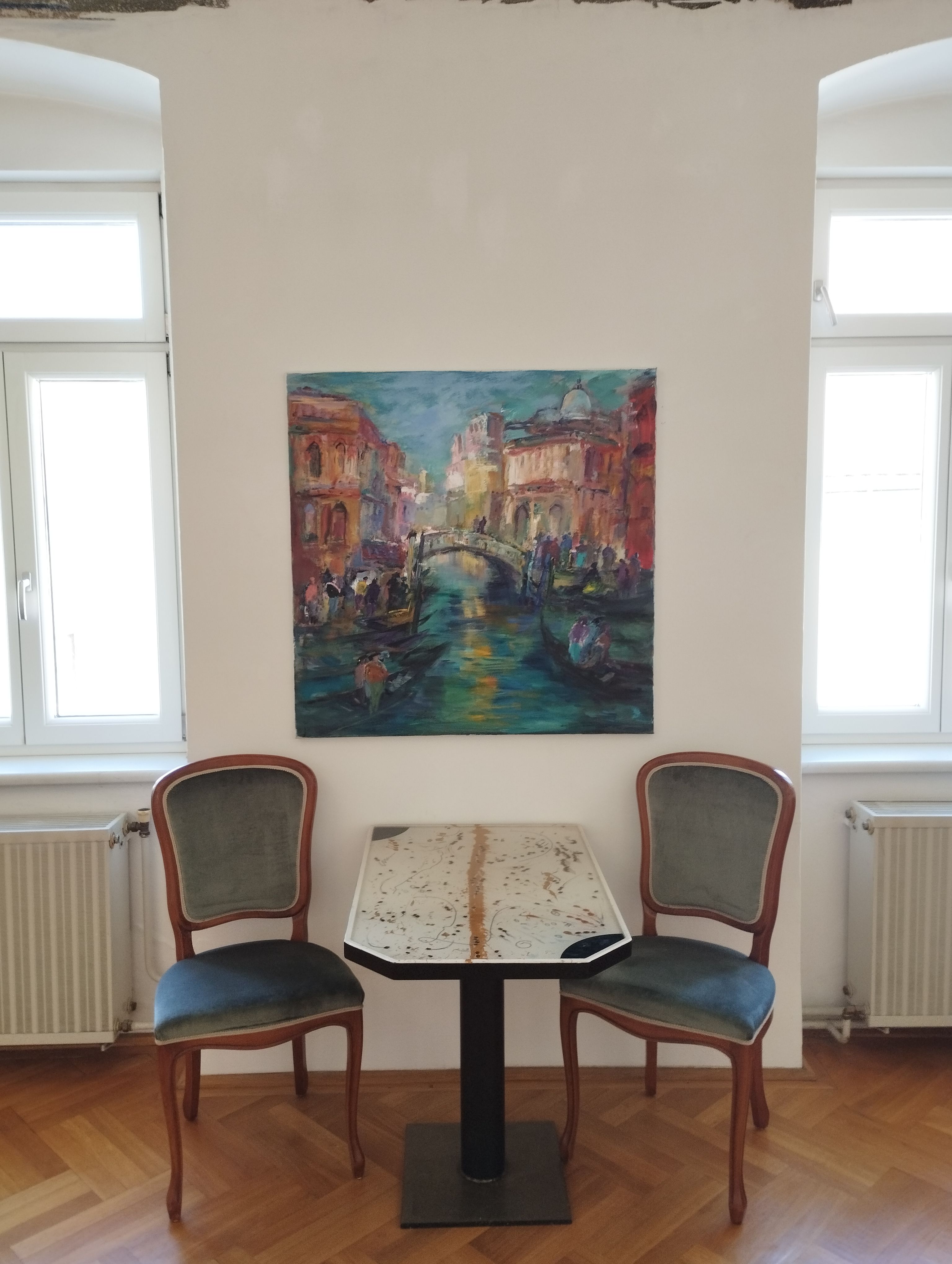 Two chairs and a table in front of a painting on a white wall.
