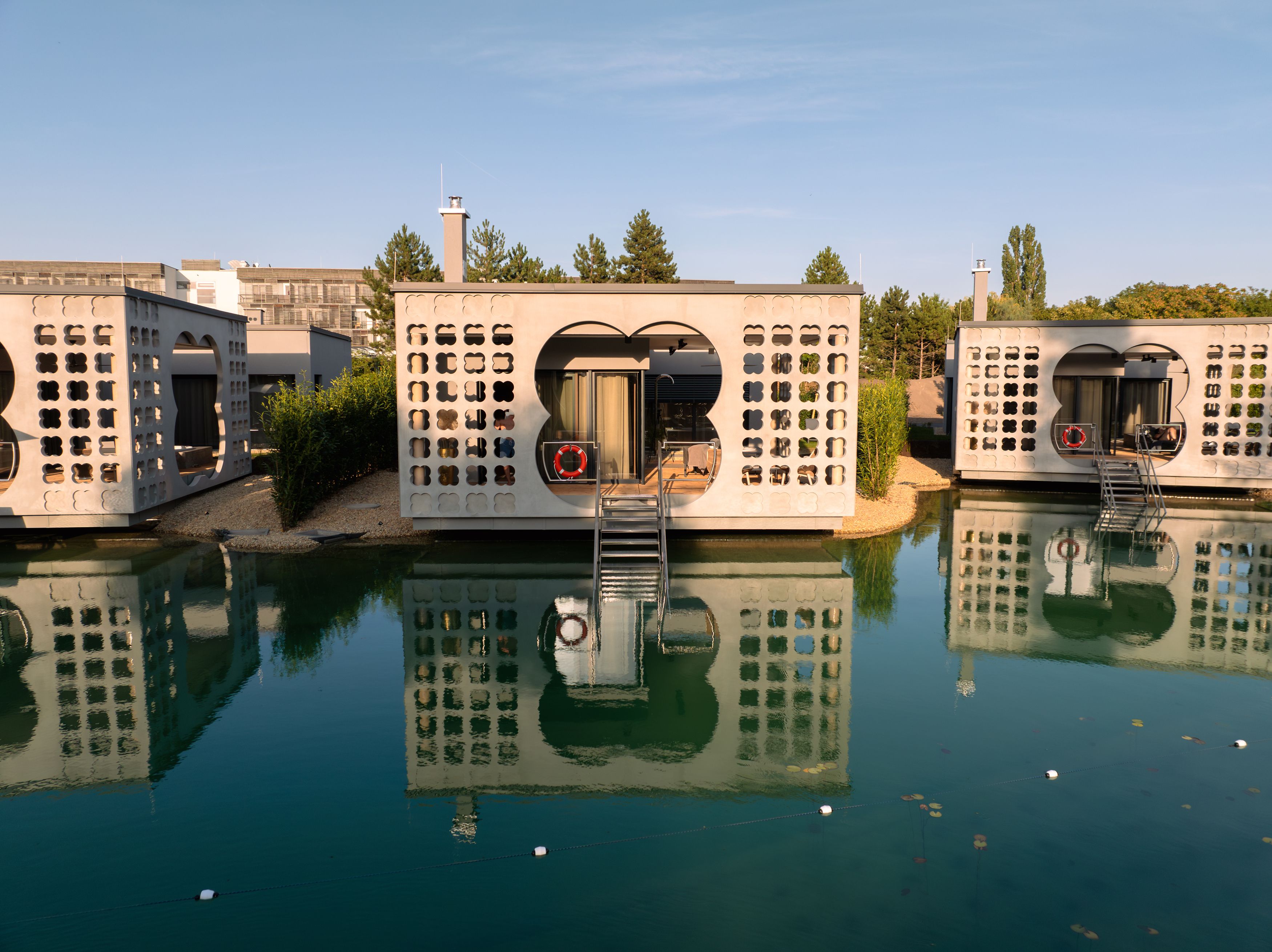 Modern villas on water with reflective facades and stairs, surrounded by nature.