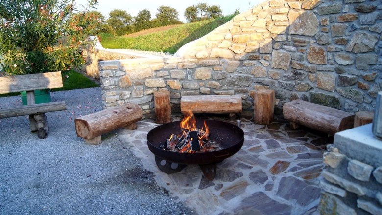 Barbecue area with fire pit and wooden benches in front of a stone wall.