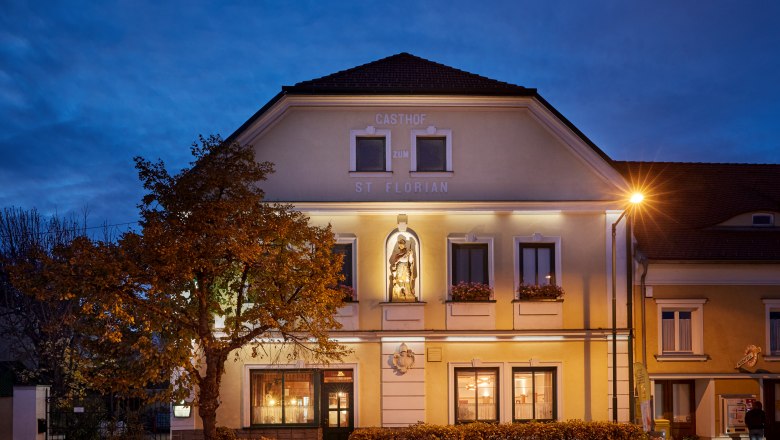St. Florian Inn at dusk with illuminated façade and statue.