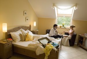 A cozy hotel room with a couple sitting at the table. The bed is unmade and a suitcase is lying open on the bed.