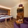 Cozy hotel room with wooden walls, double bed, TV and purple armchairs.