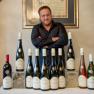 Man standing behind a row of wine bottles on a table.