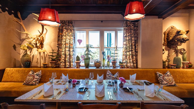 Comfortably decorated restaurant with a table setting, rustic elements and plants by the window.