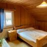 Cozy double room with wood paneling, double bed, window with blue curtains and a plant on the table.