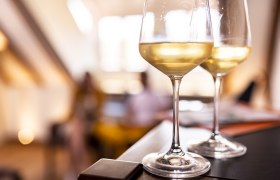 Two glasses of white wine on a table, blurred background.