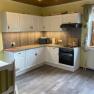 Spacious kitchen with white cupboards, stove, microwave and wooden ceiling.