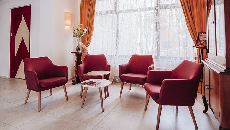 Cozy seating area with red armchairs and a small table in front of a window with curtains.