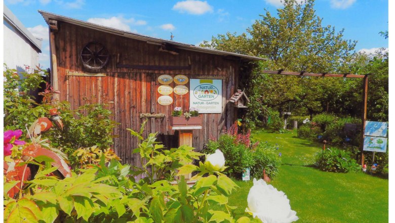 A rustic wooden building in a lush garden with signs and plants.