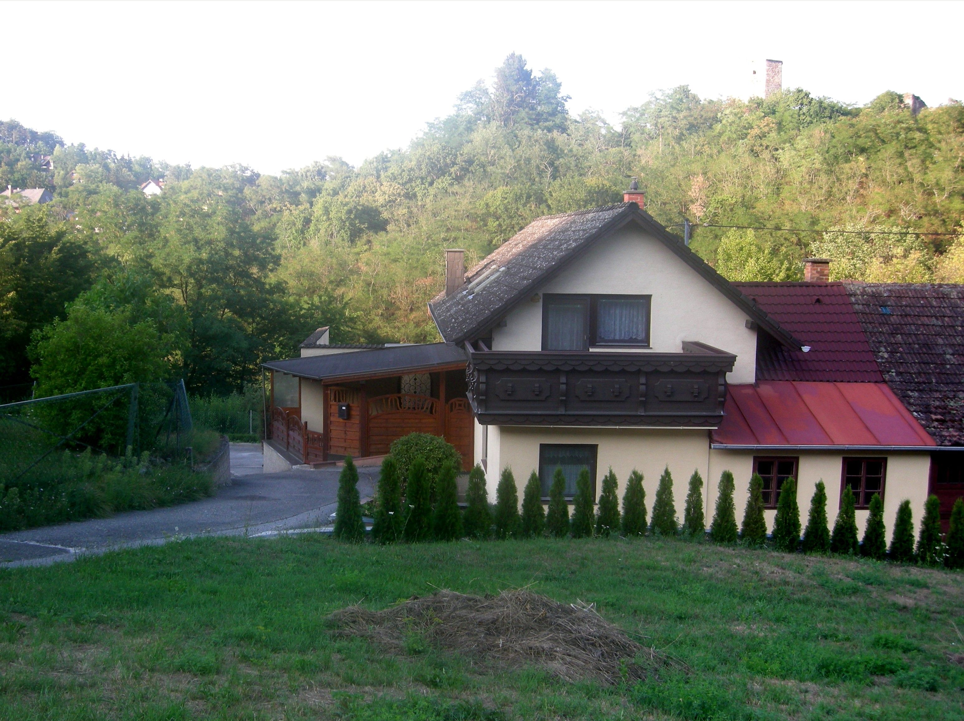 A house with a balcony and garden, surrounded by trees and hills.
