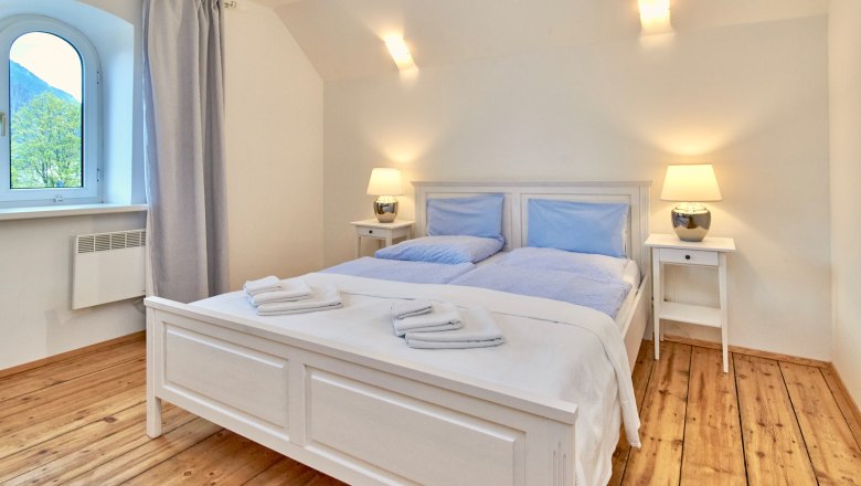 Bright bedroom with double bed, wooden floor and two bedside tables with lamps.