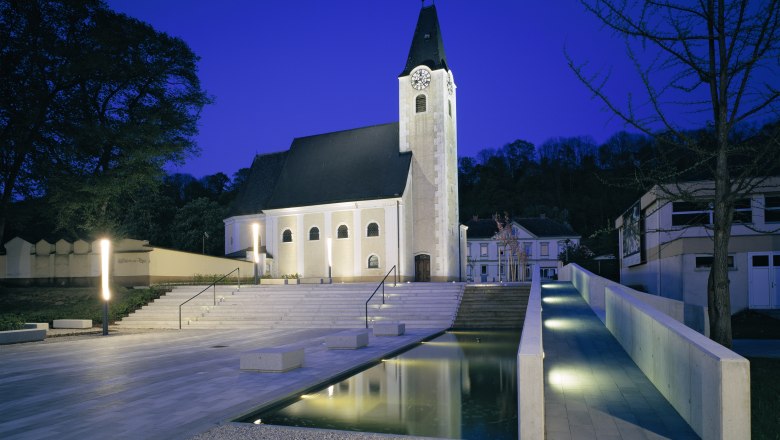 Evening shot of an illuminated church square with steps and water basin in Ernsthofen.