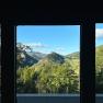 View from a window onto a green mountain landscape with a blue sky.
