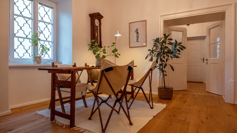 Cozy room with wooden floor, table, chairs and plants.