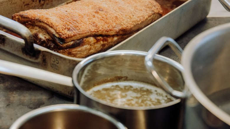 Crispy roast pork in a metal pan, pots of gravy next to it.