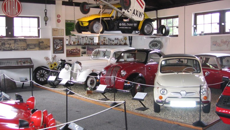 Interior view of a classic car museum with various classic cars and an airplane on the ceiling.