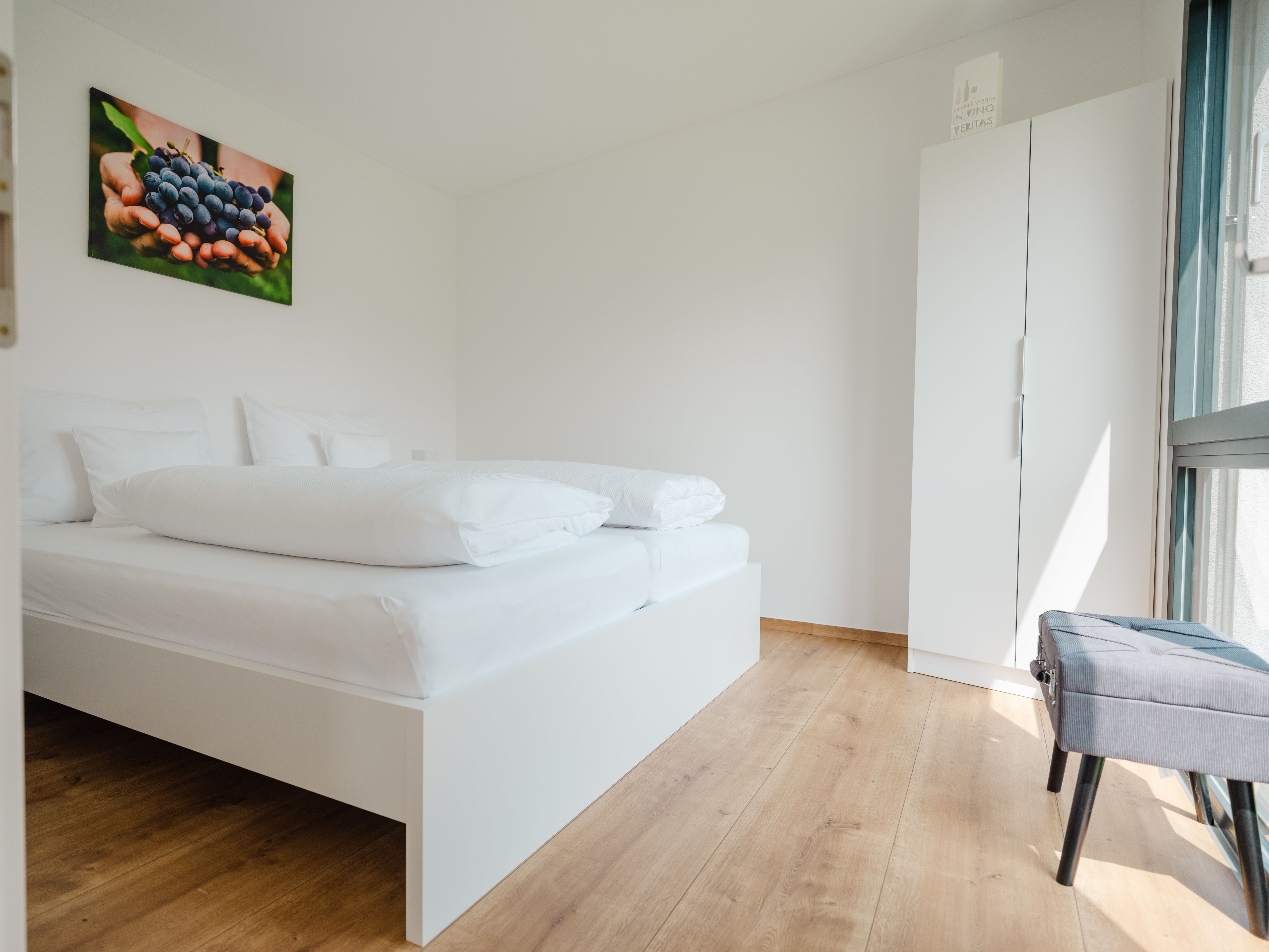 Modern bedroom with white bed, wooden floor and picture of grapes on the wall.