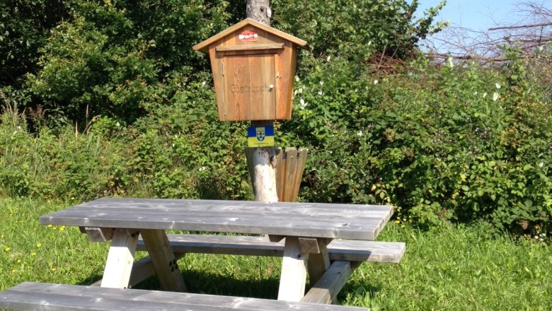 Picnic table next to a wayside shrine in a meadow with trees in the background.